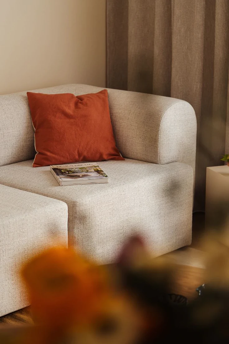 beige couch with a vibrant red cushion and a design book on the seat, creating a cozy corner